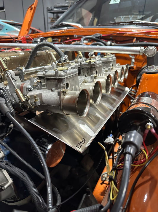 Close-up of a classic car engine with exposed carburetors and orange engine bay