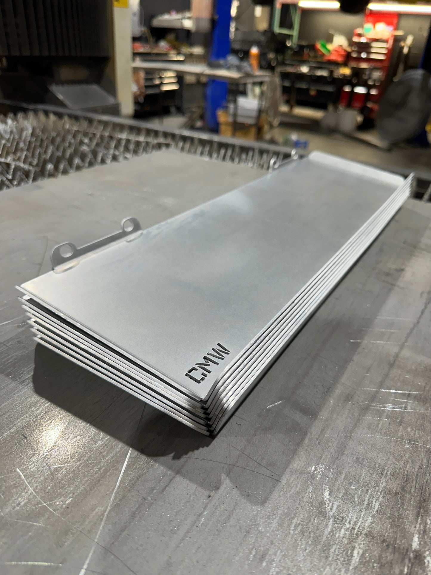 Stack of laser-cut metal plates with 'CMW' engraving in a workshop setting